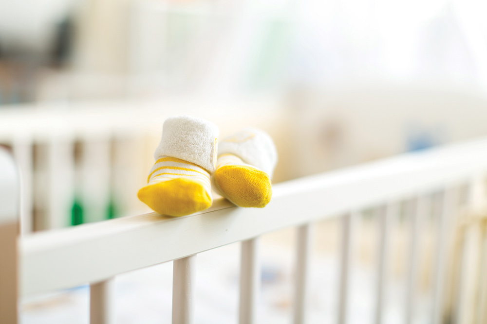 Two white and yellow baby socks sitting on top of crib rail