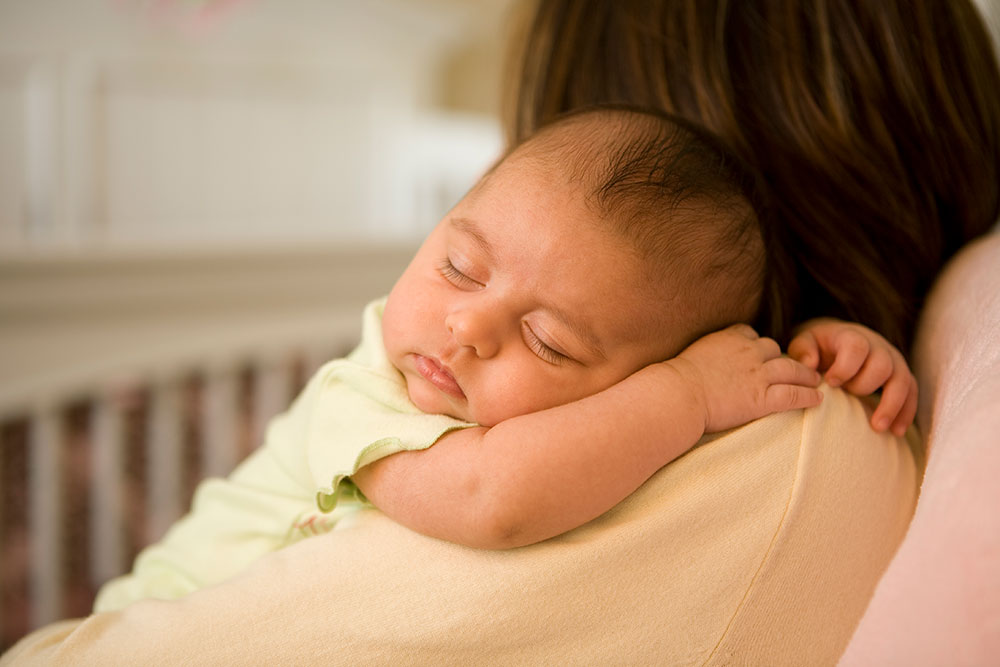 Mother seated holding young baby, with baby's head on mother's shoulder