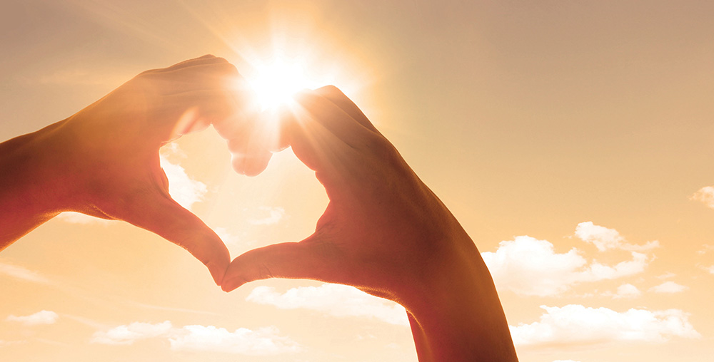 two hands making a heart shape help up towards the sun