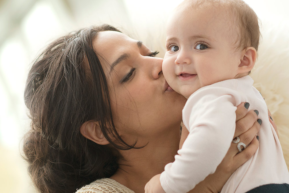 Happy mom kissing smiling baby on the cheek