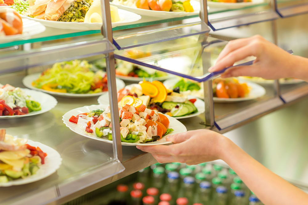 Person taking a beautiful salad dish from a cafeteria serving station with colorful fresh salad plates
