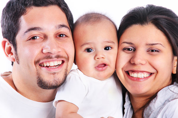 Young Latino family, smiling towards camera with baby's face nestled between father and mother's faces