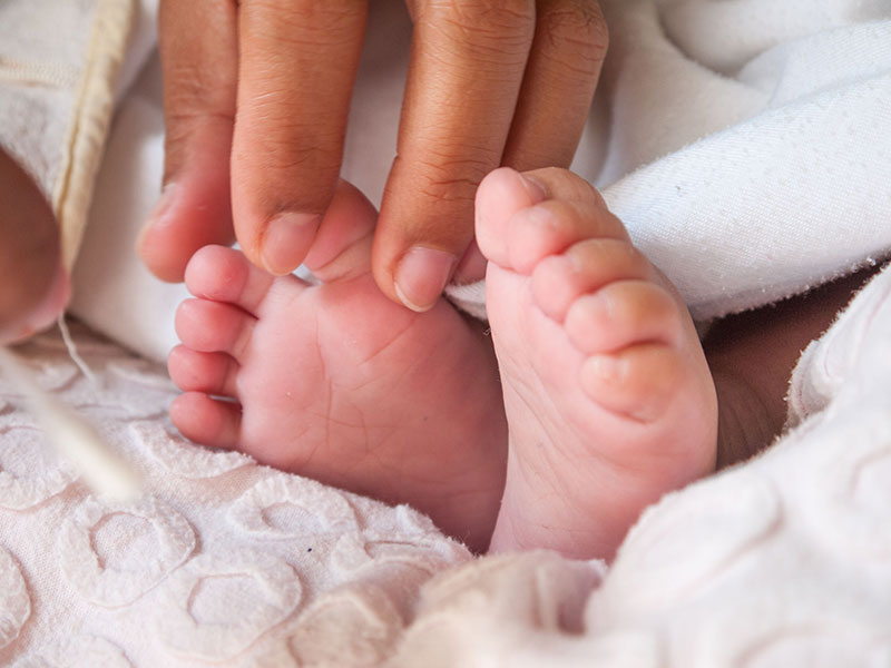Babys feet sticking out from white soft covers carefully touched by loving adult hand