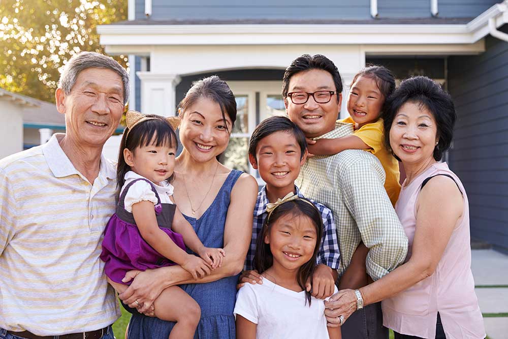 8-member smiling Asian family, 3 generations, in front of a nice traditional home, sunny day