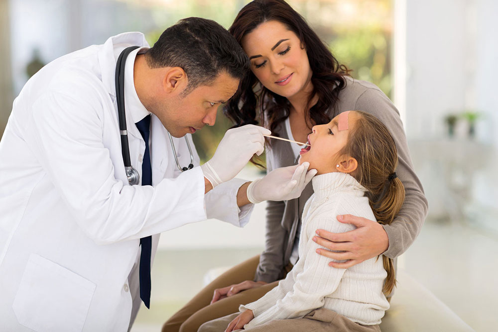Young girl getting her throat looked at by doctor while she is seated next to her mom