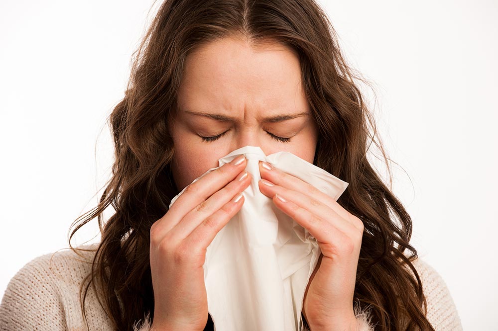 Woman sneezing into a tissue