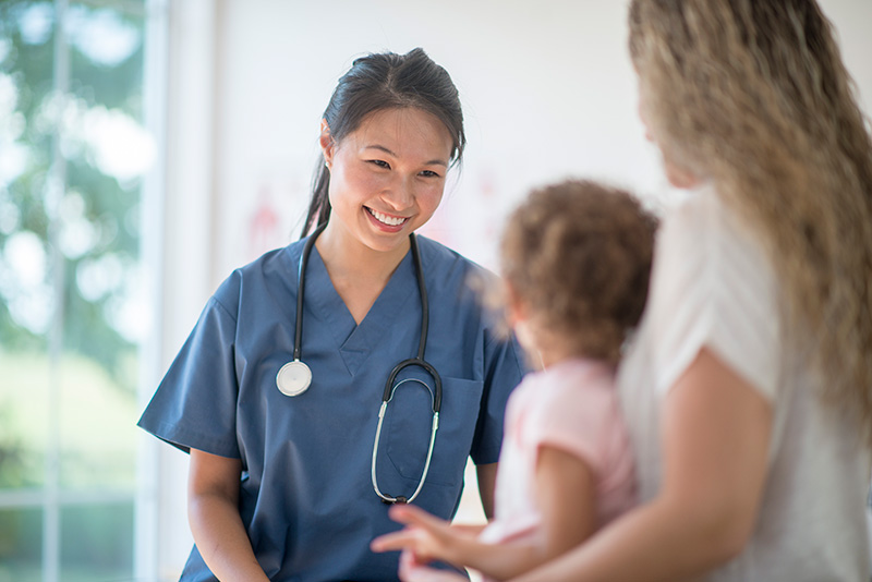 Young Asian woman doctor smiling warmly at young mother and toddler